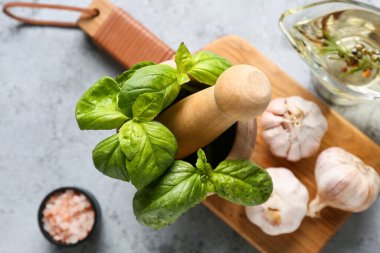 Fesleğen yapraklı ahşap havan ve gri arka planda sarımsak.