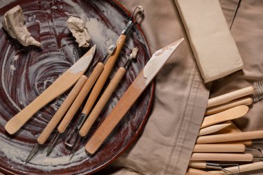 Heykeltraş aletleri seti ve önlük üzerine kil, yakın çekim.