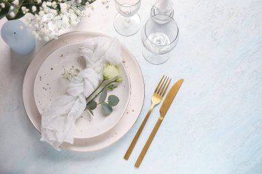 Peçete, çiçek, okaliptüs dalı ve açık mavi arka planda gözlüklü düğün masası.