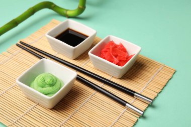 Wasabi, soya sosu ve bambu hasırı turşulu kaseler turkuaz arka planda, yakın plan