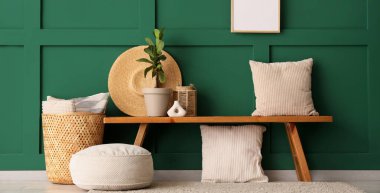 Yastıklı ahşap bank, hasır sepet ve yeşil duvarlı ev bitkisi.