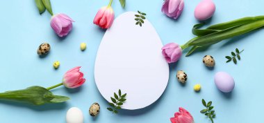 Boş kart, Paskalya yumurtası, yeşil yapraklar ve mavi arka planda çiçekler.