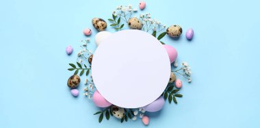 Boş kart, Paskalya yumurtası, yeşil yapraklar ve mavi arka planda çiçekler.