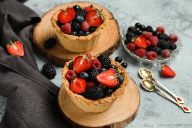 Gri arkaplanda farklı taze böğürtlenler olan tahtadan tatlı turtalar.