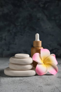 Gri grunge arka planında taş, tesisat çiçeği ve bir şişe kozmetik ürünle kaplıcaya güzel bir kompozisyon, yakın plan.