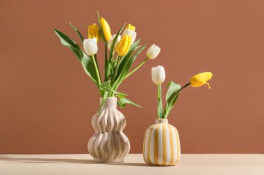 Kahverengi duvara karşı bej masanın üzerinde güzel lale çiçekleri olan vazolar.