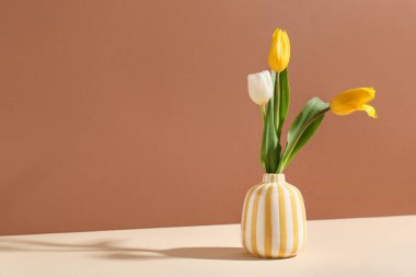 Kahverengi duvara karşı bej masanın üzerinde güzel lale çiçekleri olan vazo.