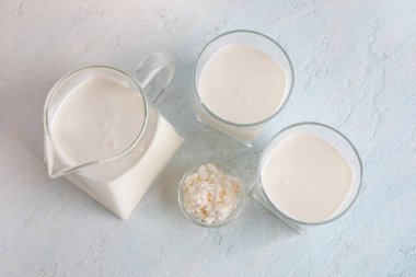 Bir bardak taze kefir ve açık mavi arka planda süzme peynirli kase.