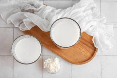 Bir bardak taze kefir ve beyaz fayanslı süzme peynirli kase.