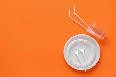 Turuncu arka planda plastik plakalar, fincanlar, pipetler ve çatal bıçak takımı