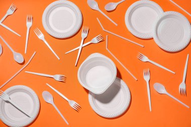 Turuncu arka planda plastik tabak, kase ve çatal bıçak takımı.