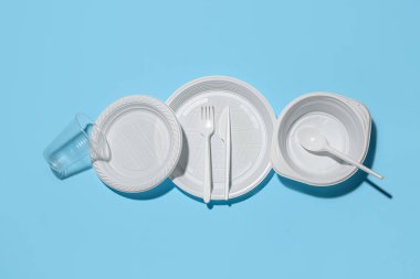 Plastik tabaklar, fincan, kase ve çatal bıçak takımı mavi arka planda.