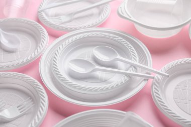 Plastik tabaklar, fincanlar, kase ve pembe arka planda çatal bıçak.