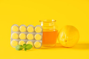 Limonlu öksürük pastili, nane yaprağı ve sarı arka planda bal kavanozu.