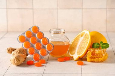 Limonlu öksürük damlaları, nane yaprakları, zencefil kökü ve beyaz fayanslı bal kavanozu.