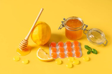 Limonlu öksürük damlaları, sarı arka planda bal kavanozu ve nane yaprakları