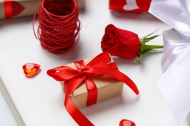 Kırmızı gül ve iplik içeren hediye kutusu beyaz masada, yakın plan. Sevgililer Günü kutlaması