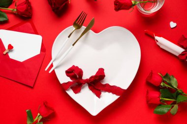 Kırmızı zemin üzerinde gül çiçekleri, mumlar, kağıt kartlar ve zarfla Sevgililer Günü için masa ayarı