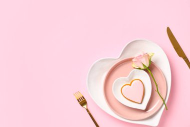 Sevgililer Günü için güzel bir masa, lezzetli kurabiyeler ve pembe arka planda gül çiçekleri.
