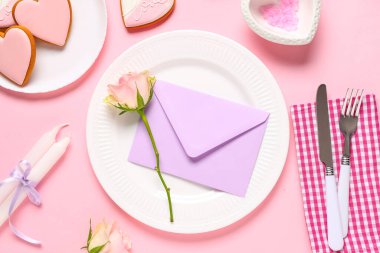 Tatlı kurabiyeler, mumlar, zarf ve pembe arka planda gül çiçekleriyle Sevgililer Günü için güzel bir masa.