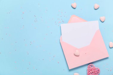 Zarflı kompozisyon, konfeti, dekoratif kalpler ve mavi arka planda boş bir kart. Sevgililer Günü kutlaması