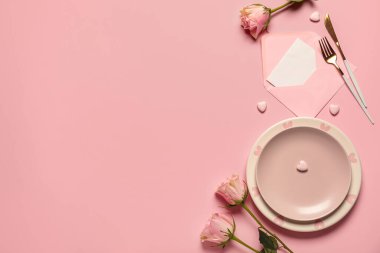 Gül çiçekleri, zarf ve pembe arka planda kağıt kartla Sevgililer Günü için güzel bir masa.