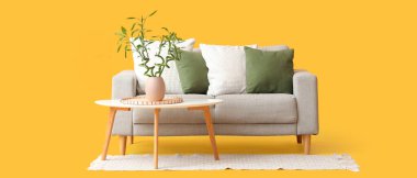 Vazoda bambu saplı masa, gri kanepe ve sarı arka planda halı.