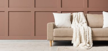 Oturma odasının iç tarafındaki kahverengi duvarın yanında ekoseli ve yastıklı rahat bir kanepe. Tasarım için pankart