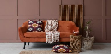 Oturma odasının iç tarafındaki kahverengi duvarın yanında rahat bir kanepe, masa, bitki ve katlanan ekran.