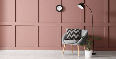 Oturma odasındaki kahverengi duvarın yanında rahat bir koltuk, bitki ve zemin lambası. Tasarım için pankart