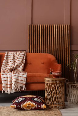 Comfortable sofa, table and folding screen near brown wall in interior of living room, closeup