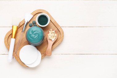 Tahta tepside bir kavanoz spirulina yüz maskesi ve beyaz ahşap arka planda malzemeler.