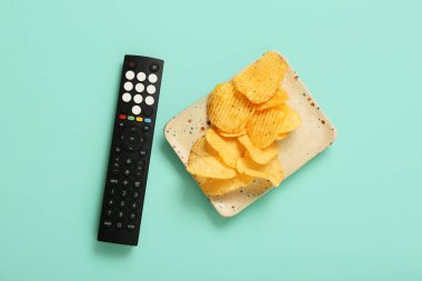Modern TV uzaktan kumandası ve turkuazda patates cipsi olan bir tabak.