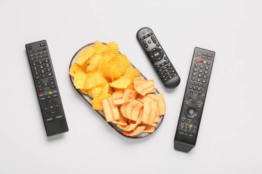 Farklı modern TV uzaktan kumandası ve gri arka planda patates cipsi tabağı.