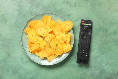Modern TV uzaktan kumandası ve yeşil grunge arka planda patates cipsi tabağı.