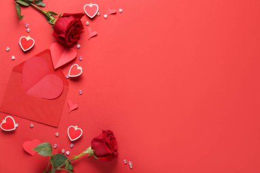 Composition with rose flowers, paper hearts and envelope on red background