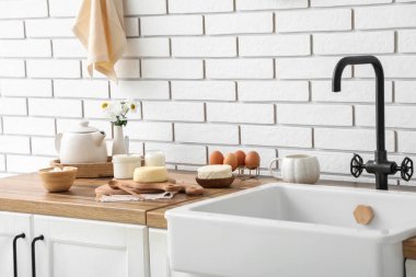 Mutfakta beyaz tuğla duvarın yanında farklı süt ürünleri var.