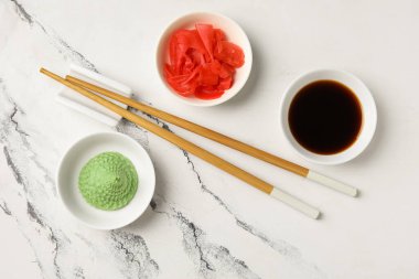 Beyaz arka planda wasabi, soya sosu ve zencefil turşusu olan kaseler.