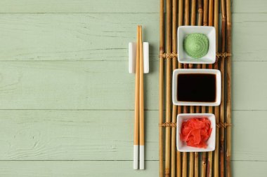 Bowls with wasabi, soy sauce and pickled ginger on green wooden background