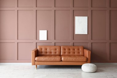 İçinde puf olan kanepe ve odadaki kahverengi duvarda resimler.