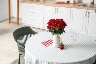 Mutfaktaki yemek masasının üstünde kırmızı güller olan vazo Sevgililer Günü için süslenmiş.