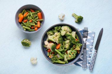 Bir kase karışık sebze ve açık mavi arka planda çatal bıçak