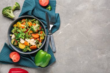 Bir kase haşlanmış karışık sebze ve gri arka planda çatal bıçak.