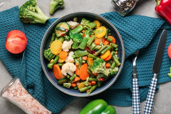 Bir kase haşlanmış karışık sebze ve gri arka planda çatal bıçak.