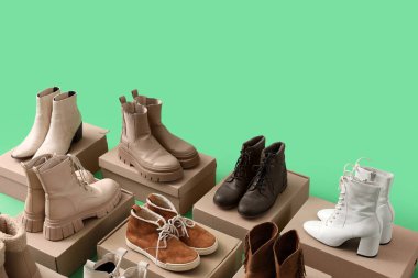 Yeşil arka planda ayakkabı kutuları olan farklı kış botları.