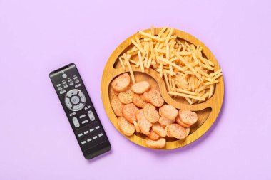 Çıtır çıtır atıştırmalık ahşap tabak ve mor arka planda modern TV uzaktan kumandası.