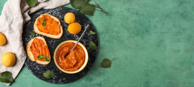 Bir kase lezzetli kayısı reçeli ve yeşil grunge arka planda dilimlenmiş ekmek.