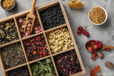 Gri grunge arka planında farklı çeşit kuru çay içeren ahşap kutu, yakın plan.