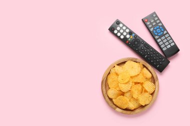 Farklı modern TV uzaktan kumandası ve pembe arka planda patates cipsi.