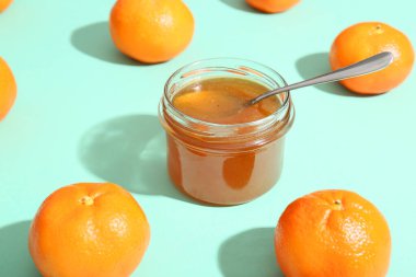 Turkuaz arka planda kaşıkla lezzetli mandalina reçeli kavanozu
